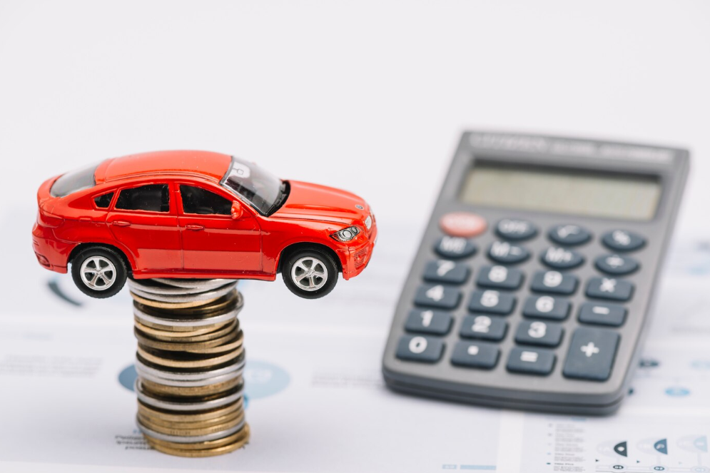 imagem ilustrativa de refinanciamento de veículo com carro de brinquedo sobre pilha de moedas e calculadora ao lado