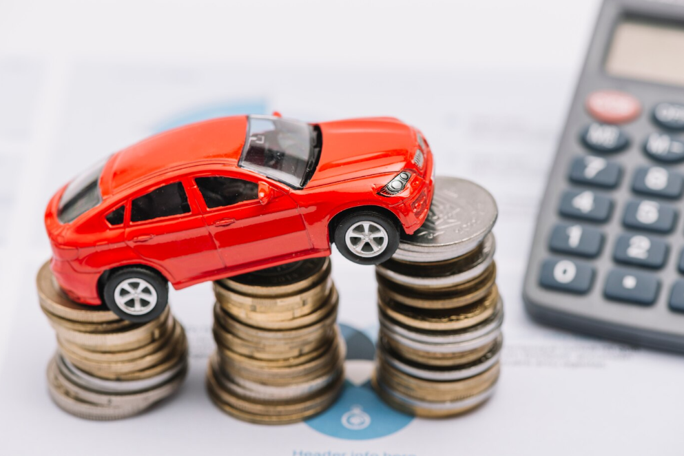 imagem ilustrativa de refinanciamento de veículo com carro de brinquedo sobre pilhas de moedas e calculadora ao lado
